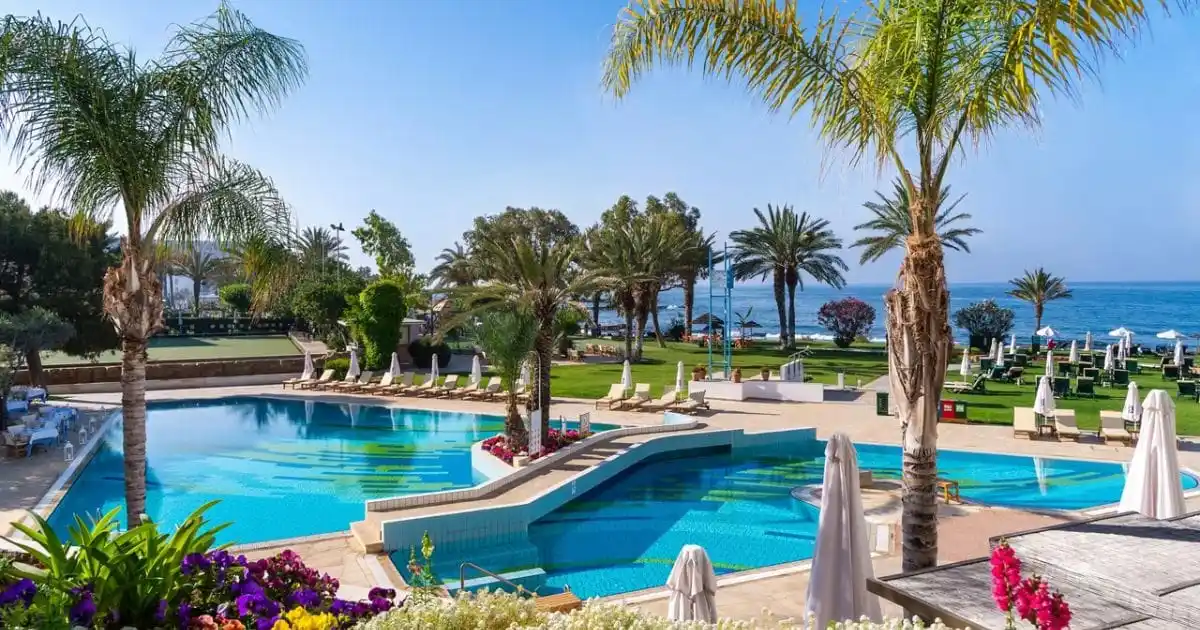 The outdoor swimming pool complex, palm trees and beachfront gardens at the Athena Royal Beach Hotel in Paphos, Cyprus.