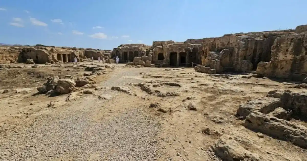 The open, unshaded, and rocky terrain at the Tombs of the Kings archaeological site in Paphos, Cyprus showing paths leading to excavated anchient rock-cut burial chambers under a bright, unshaded sky.